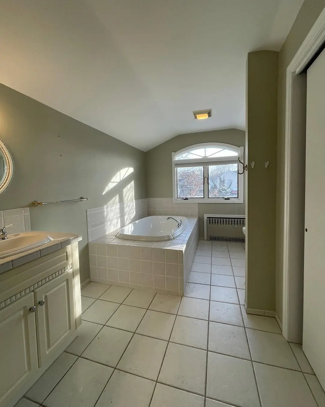 Arched window over white tiled bathtub